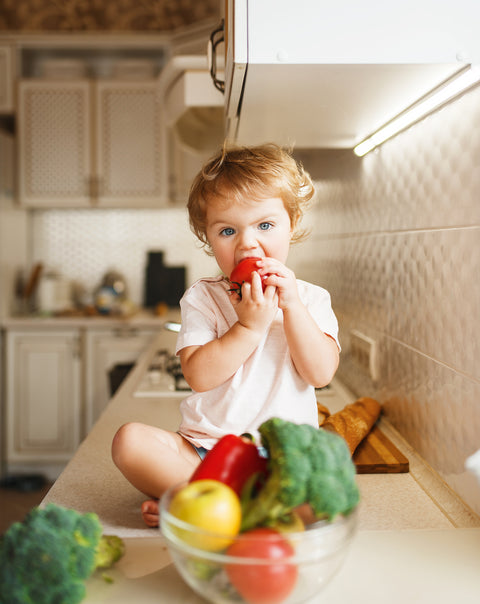 small child sitting on a counter top eating fresh vegetables out of a bowl